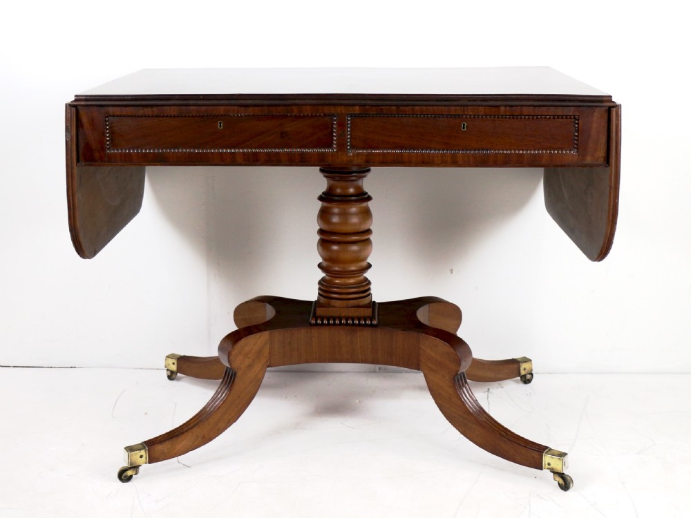 A Regency mahogany drop-leaf sofa table with frieze drawers, turned pedestal, reeded quadrupod legs, and brass castors. View V