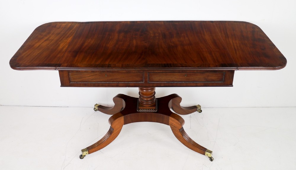 A Regency mahogany drop-leaf sofa table with frieze drawers, turned pedestal, reeded quadrupod legs, and brass castors. View IX