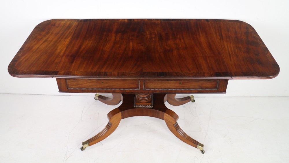 A Regency mahogany drop-leaf sofa table with frieze drawers, turned pedestal, reeded quadrupod legs, and brass castors. View XI