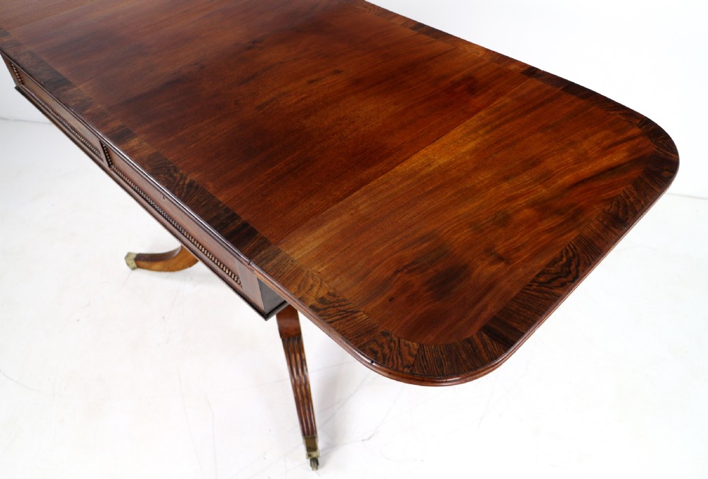 A Regency mahogany drop-leaf sofa table with frieze drawers, turned pedestal, reeded quadrupod legs, and brass castors. View XII