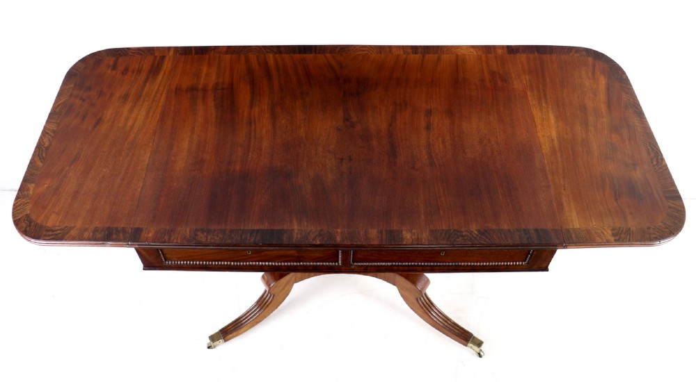 A Regency mahogany drop-leaf sofa table with frieze drawers, turned pedestal, reeded quadrupod legs, and brass castors. View XV
