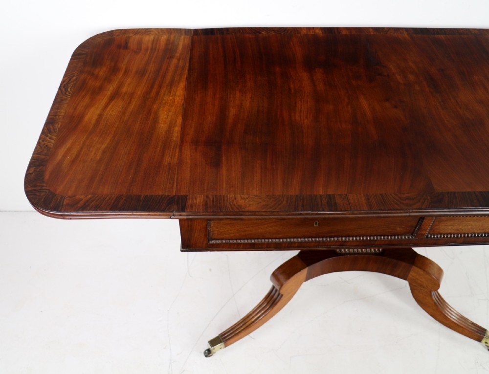 A Regency mahogany drop-leaf sofa table with frieze drawers, turned pedestal, reeded quadrupod legs, and brass castors. View XVI