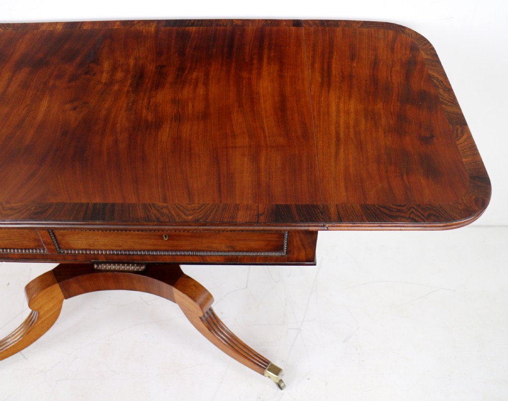 A Regency mahogany drop-leaf sofa table with frieze drawers, turned pedestal, reeded quadrupod legs, and brass castors. View XVII