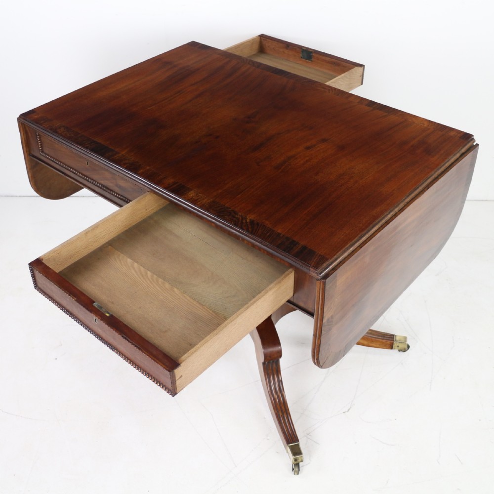 A Regency mahogany drop-leaf sofa table with frieze drawers, turned pedestal, reeded quadrupod legs, and brass castors. View XX