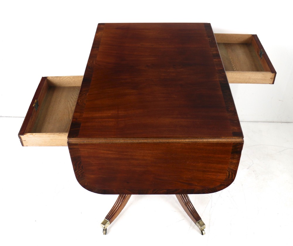 A Regency mahogany drop-leaf sofa table with frieze drawers, turned pedestal, reeded quadrupod legs, and brass castors. View XXI