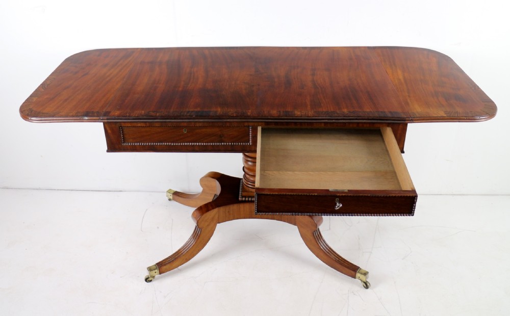 A Regency mahogany drop-leaf sofa table with frieze drawers, turned pedestal, reeded quadrupod legs, and brass castors. View XXII
