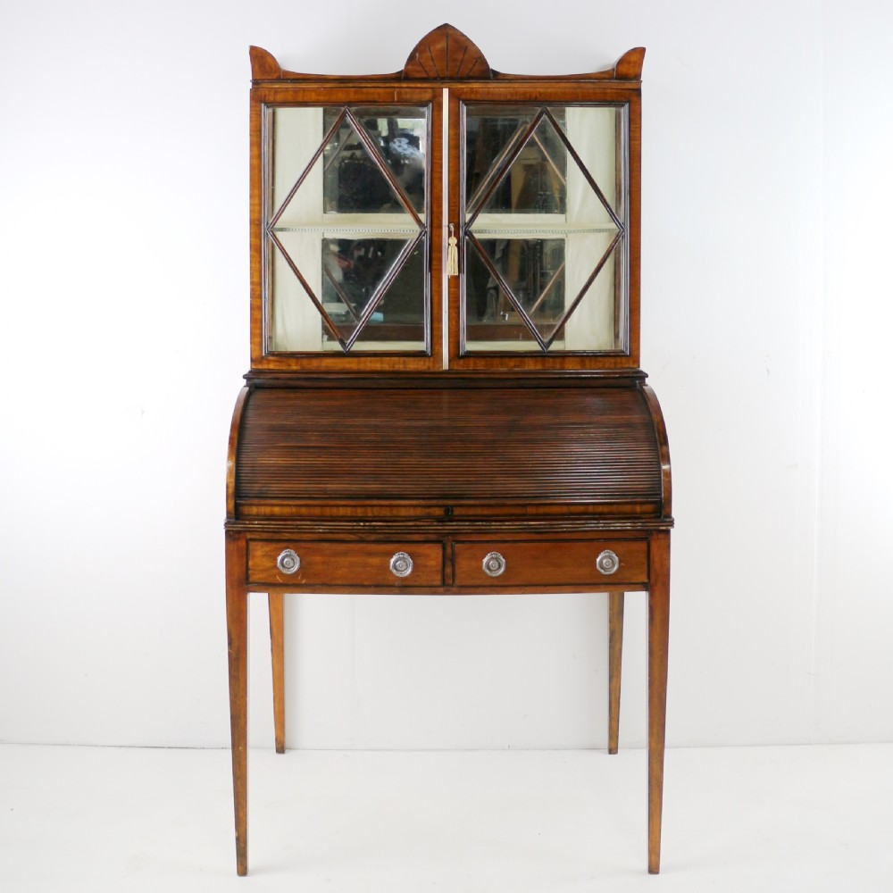 An antique mahogany writing desk cabinet featuring an upper glass cabinet with diamond glazing bars, a curved slatted tambour shutter section, and two drawers on square tapered legs.