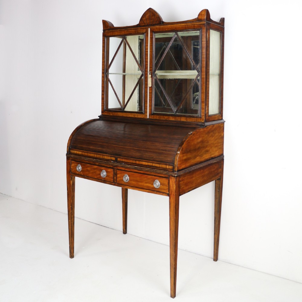 An antique mahogany writing desk cabinet featuring an upper glass cabinet with diamond glazing bars, a curved slatted tambour shutter section, and two drawers on square tapered legs. View III