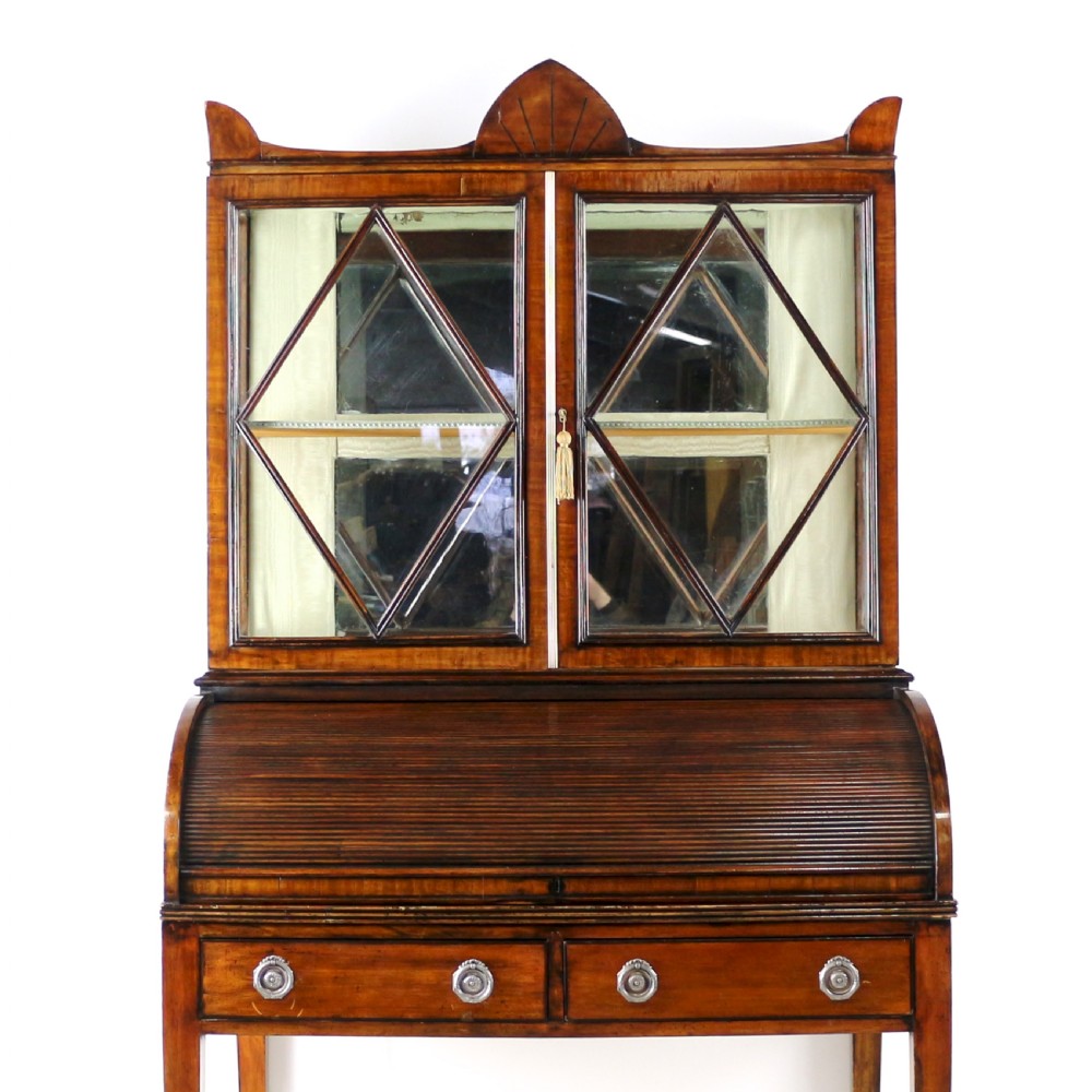 An antique mahogany writing desk cabinet featuring an upper glass cabinet with diamond glazing bars, a curved slatted tambour shutter section, and two drawers on square tapered legs. View V