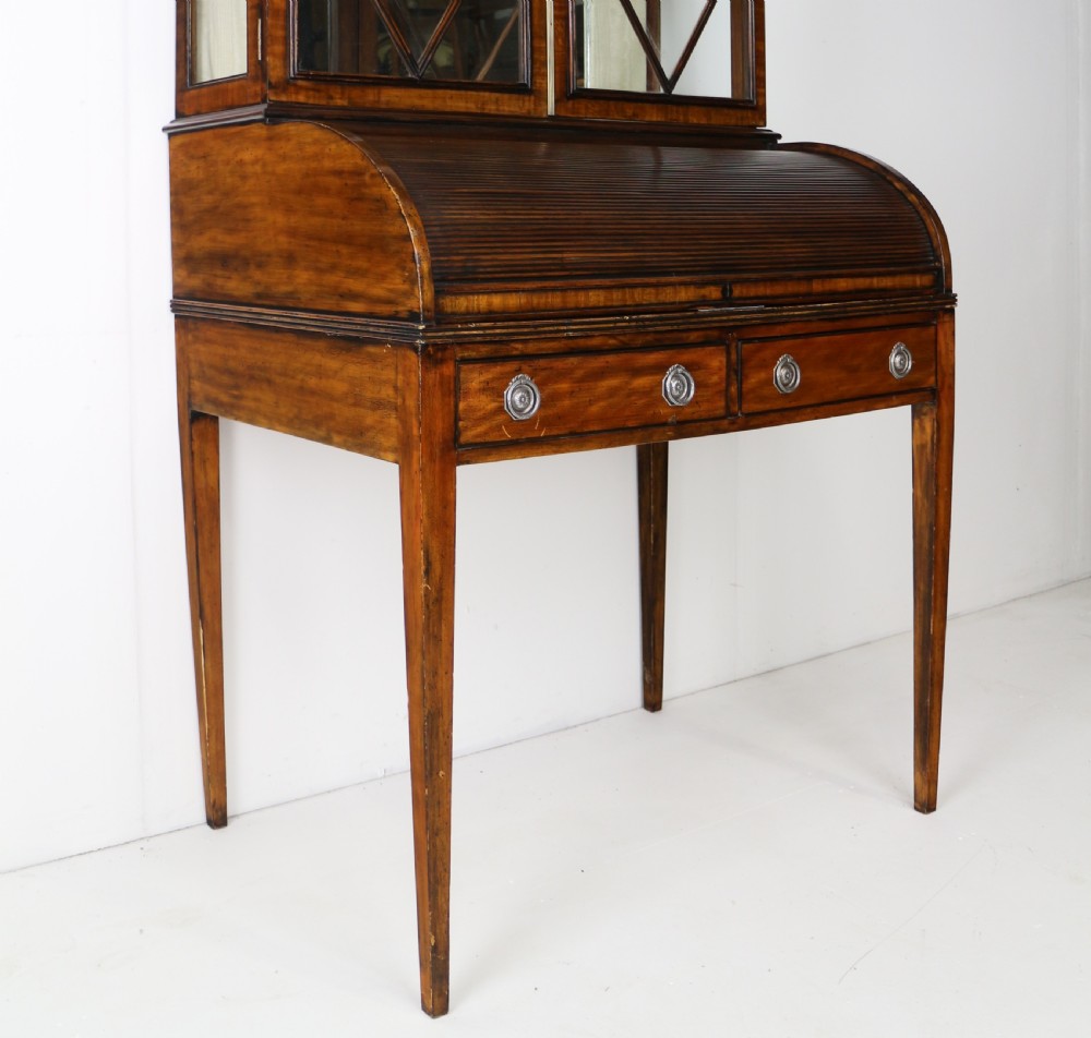 An antique mahogany writing desk cabinet featuring an upper glass cabinet with diamond glazing bars, a curved slatted tambour shutter section, and two drawers on square tapered legs. View VIII