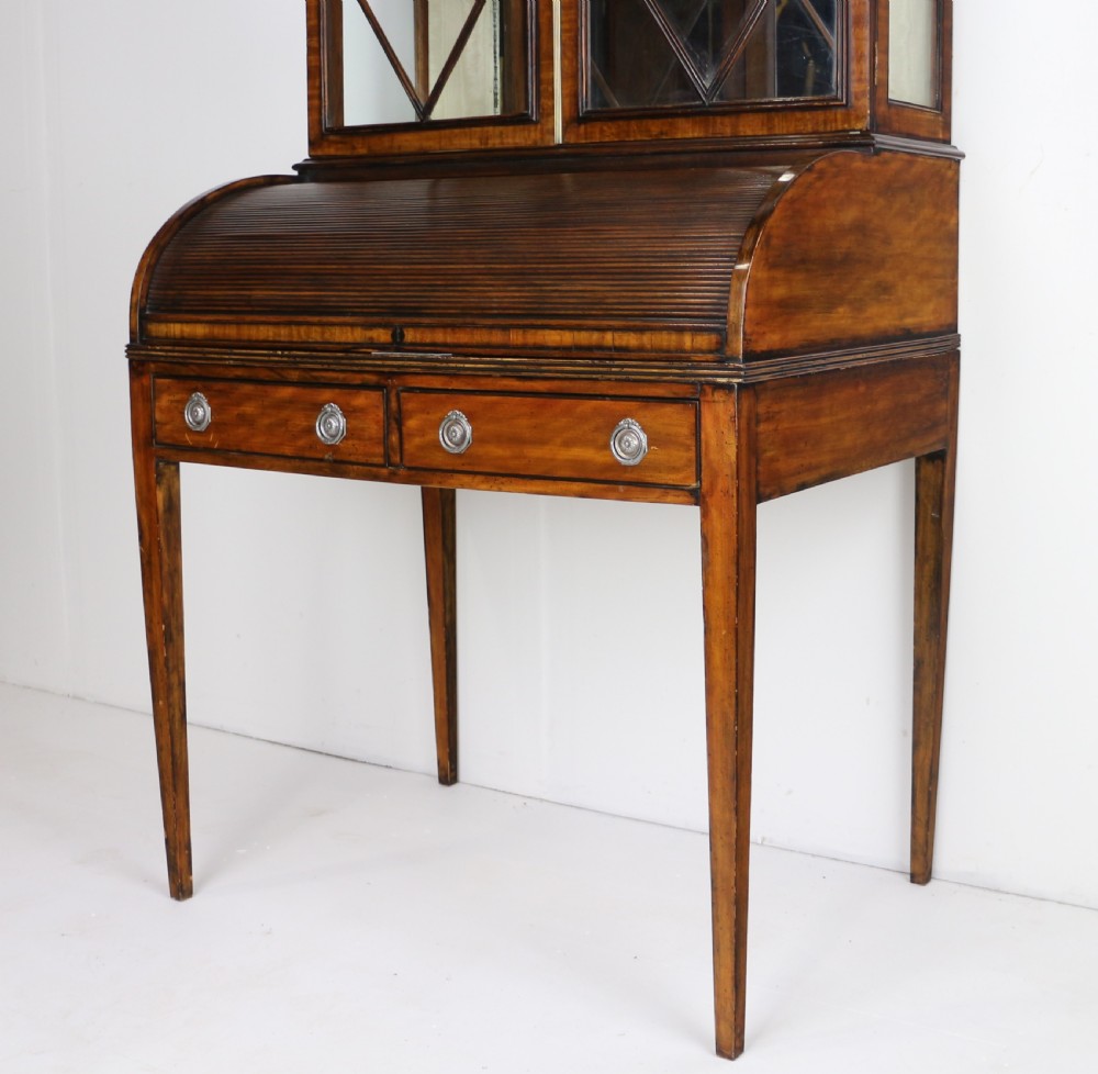 An antique mahogany writing desk cabinet featuring an upper glass cabinet with diamond glazing bars, a curved slatted tambour shutter section, and two drawers on square tapered legs. View IX