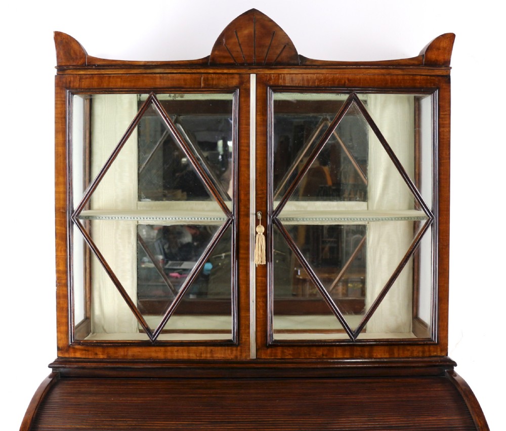 An antique mahogany writing desk cabinet featuring an upper glass cabinet with diamond glazing bars, a curved slatted tambour shutter section, and two drawers on square tapered legs. View XI