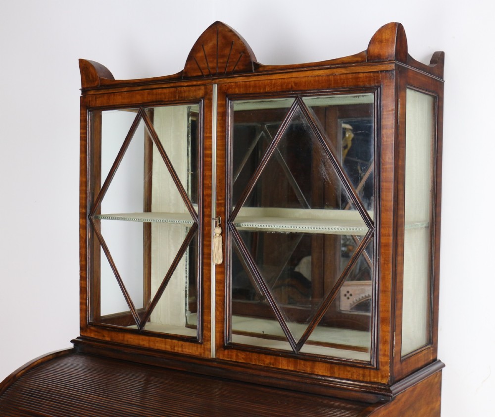 An antique mahogany writing desk cabinet featuring an upper glass cabinet with diamond glazing bars, a curved slatted tambour shutter section, and two drawers on square tapered legs. View XIV