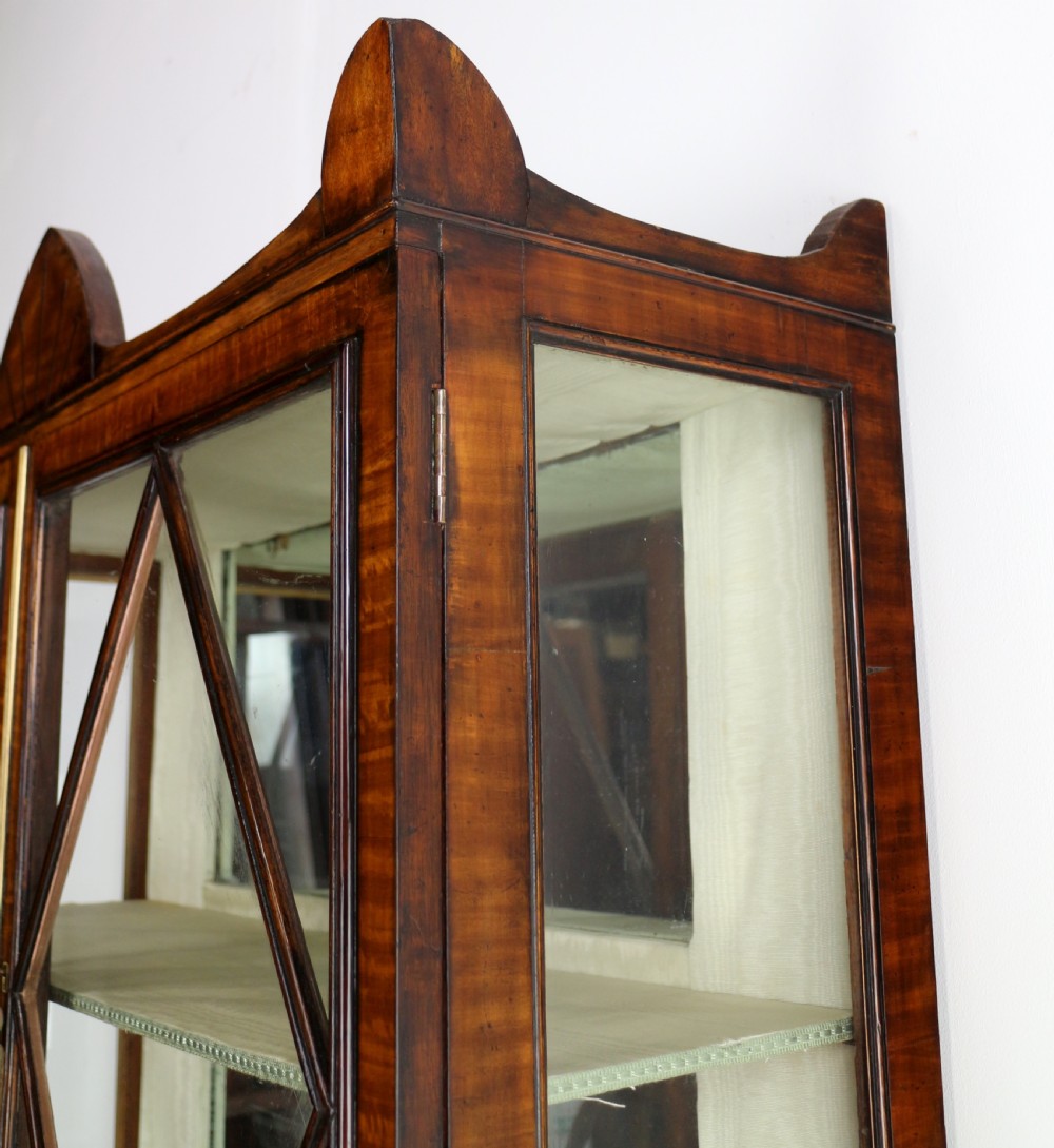 An antique mahogany writing desk cabinet featuring an upper glass cabinet with diamond glazing bars, a curved slatted tambour shutter section, and two drawers on square tapered legs. View XV