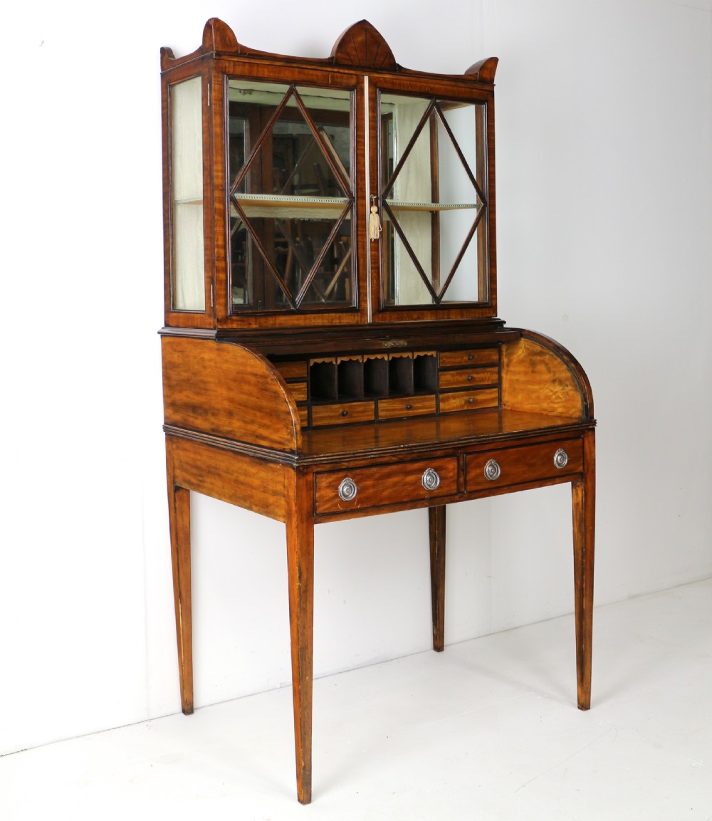 An antique mahogany writing desk cabinet featuring an upper glass cabinet with diamond glazing bars, a curved slatted tambour shutter section, and two drawers on square tapered legs. View XIX