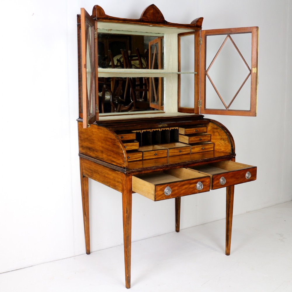 An antique mahogany writing desk cabinet featuring an upper glass cabinet with diamond glazing bars, a curved slatted tambour shutter section, and two drawers on square tapered legs. View XX