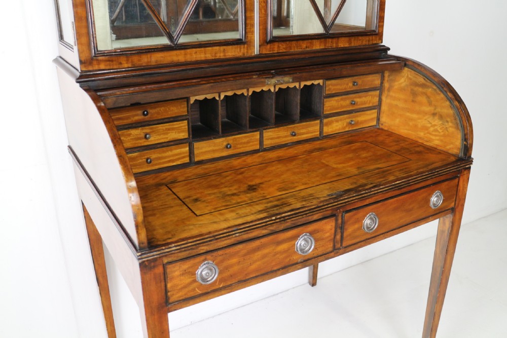 An antique mahogany writing desk cabinet featuring an upper glass cabinet with diamond glazing bars, a curved slatted tambour shutter section, and two drawers on square tapered legs. View XXII