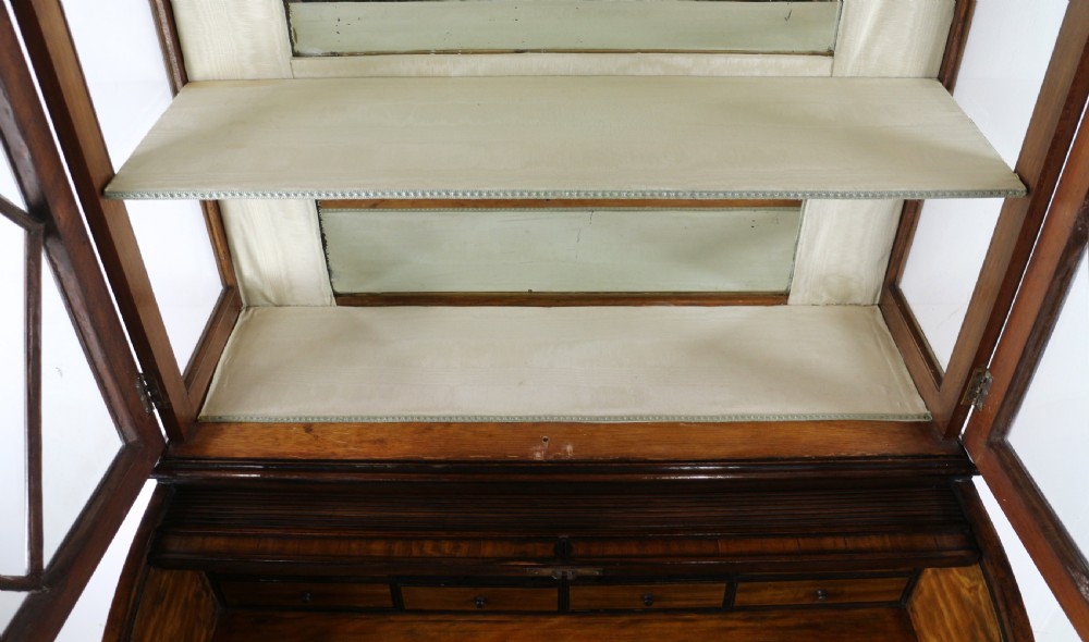 An antique mahogany writing desk cabinet featuring an upper glass cabinet with diamond glazing bars, a curved slatted tambour shutter section, and two drawers on square tapered legs. View XXIV