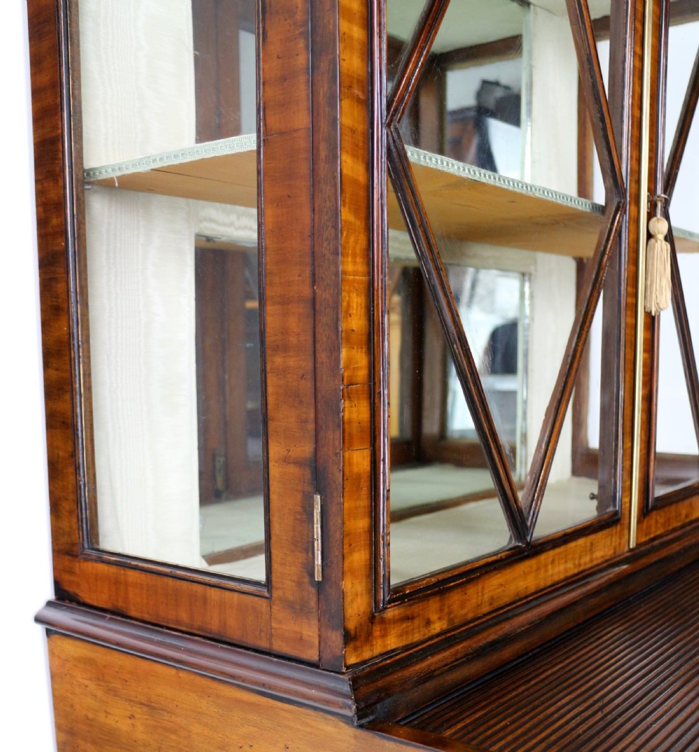 An antique mahogany writing desk cabinet featuring an upper glass cabinet with diamond glazing bars, a curved slatted tambour shutter section, and two drawers on square tapered legs. View XXVII