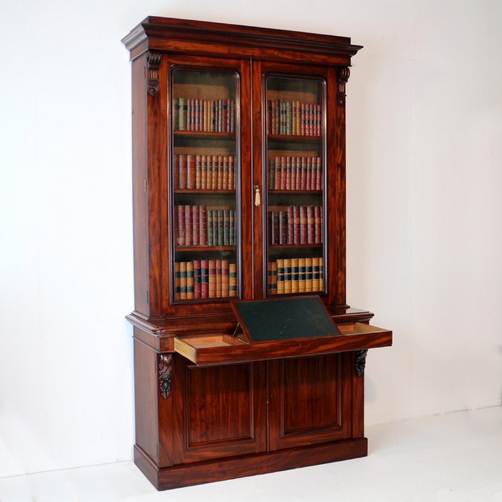 A tall William IV Cuban mahogany bookcase featuring a glazed two-door upper section with shelving above a two-door panelled cupboard base with carved side corbels. View III