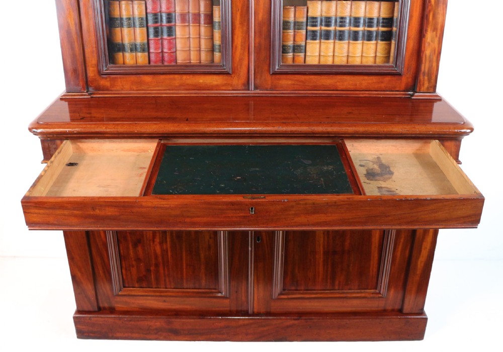 A tall William IV Cuban mahogany bookcase featuring a glazed two-door upper section with shelving above a two-door panelled cupboard base with carved side corbels. View XVII