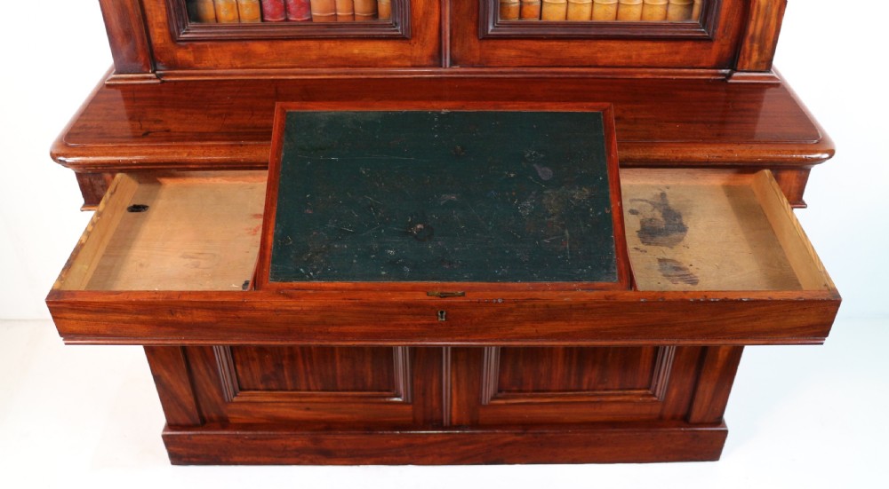 A tall William IV Cuban mahogany bookcase featuring a glazed two-door upper section with shelving above a two-door panelled cupboard base with carved side corbels. View XVIII