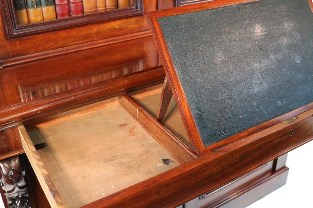 A tall William IV Cuban mahogany bookcase featuring a glazed two-door upper section with shelving above a two-door panelled cupboard base with carved side corbels. View XIX
