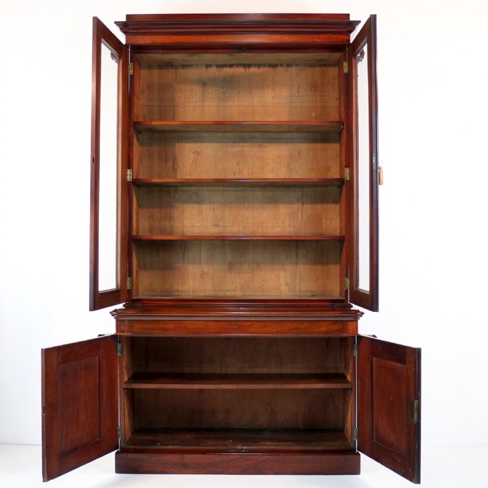 A tall William IV Cuban mahogany bookcase featuring a glazed two-door upper section with shelving above a two-door panelled cupboard base with carved side corbels. View XXII