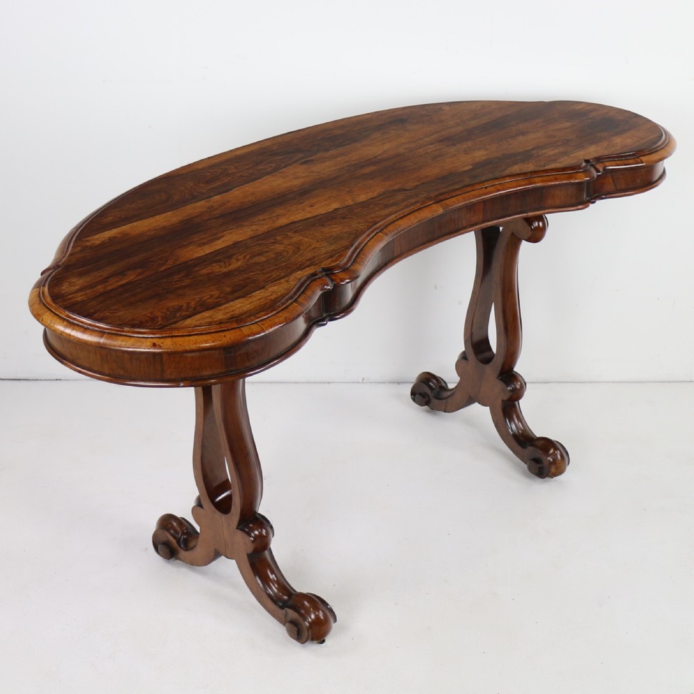 A Victorian rosewood kidney-shaped writing table with a figured timber top supported by carved lyre legs ending in scroll feet.