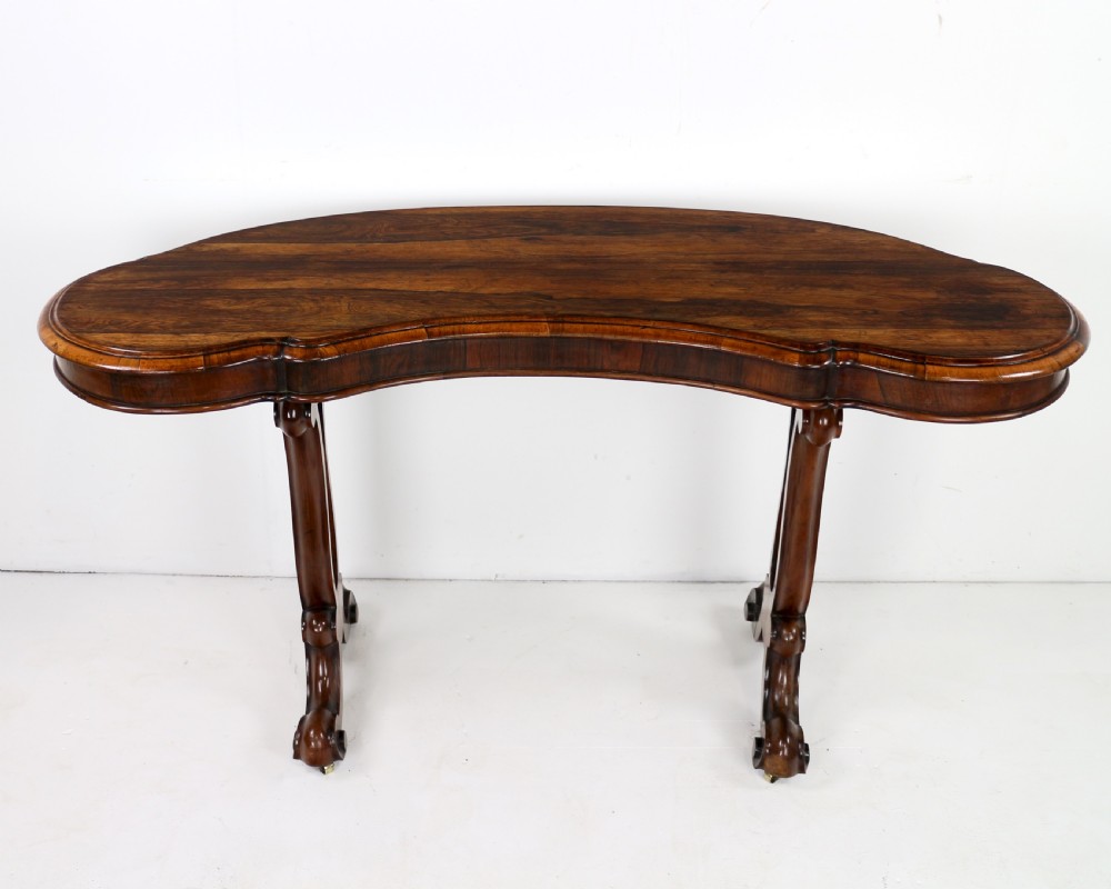 A Victorian rosewood kidney-shaped writing table with a figured timber top supported by carved lyre legs ending in scroll feet. View V