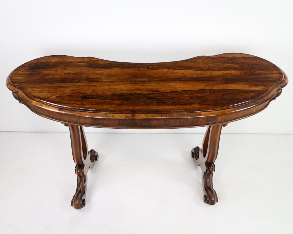 A Victorian rosewood kidney-shaped writing table with a figured timber top supported by carved lyre legs ending in scroll feet. View VI