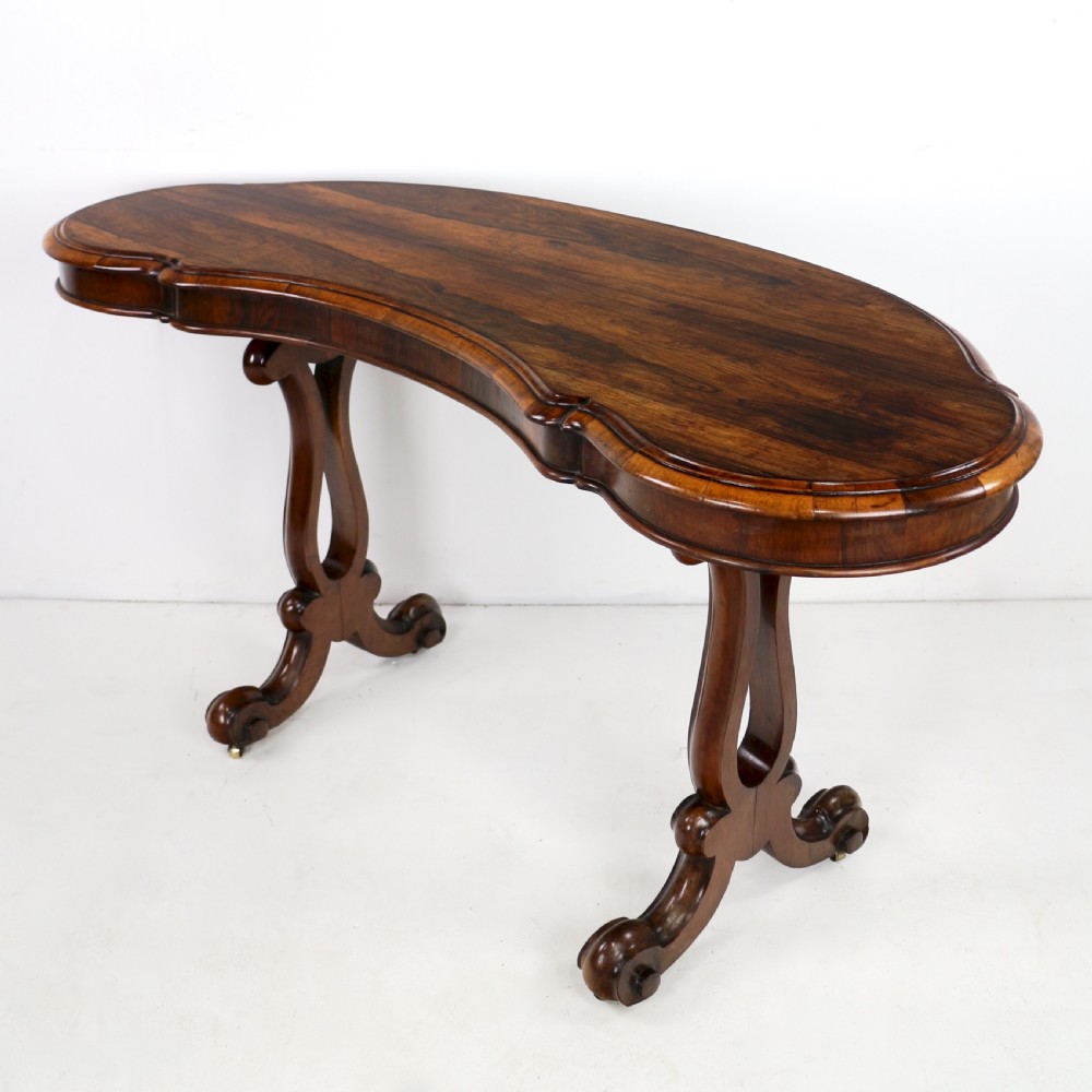 A Victorian rosewood kidney-shaped writing table with a figured timber top supported by carved lyre legs ending in scroll feet. View VII