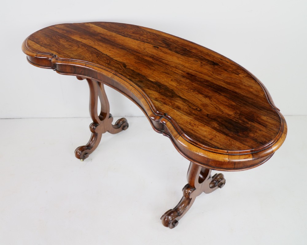 A Victorian rosewood kidney-shaped writing table with a figured timber top supported by carved lyre legs ending in scroll feet. View VIII