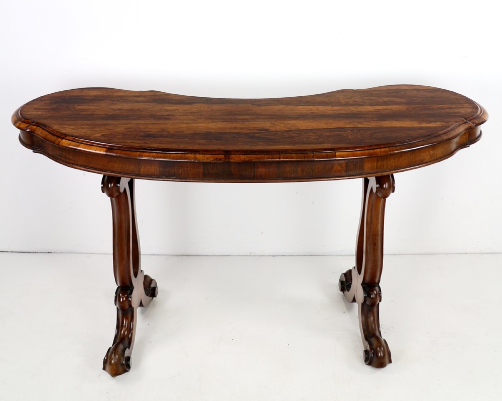 A Victorian rosewood kidney-shaped writing table with a figured timber top supported by carved lyre legs ending in scroll feet. View IX