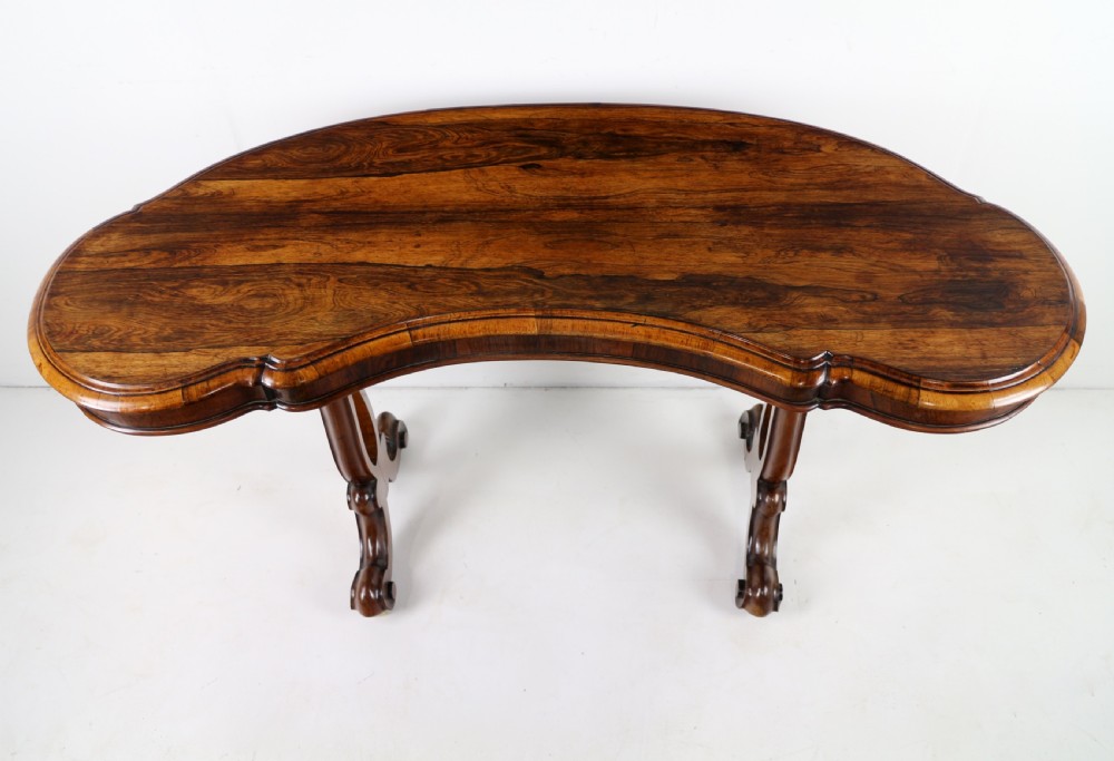 A Victorian rosewood kidney-shaped writing table with a figured timber top supported by carved lyre legs ending in scroll feet. View X
