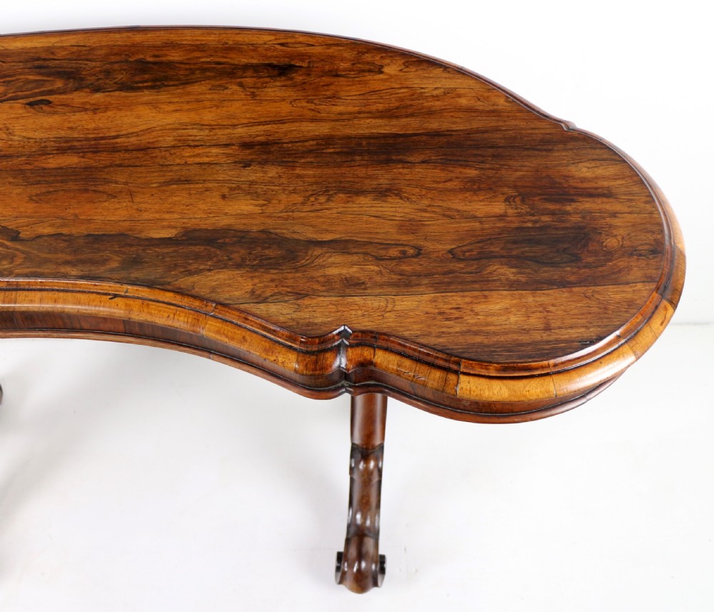 A Victorian rosewood kidney-shaped writing table with a figured timber top supported by carved lyre legs ending in scroll feet. View XII