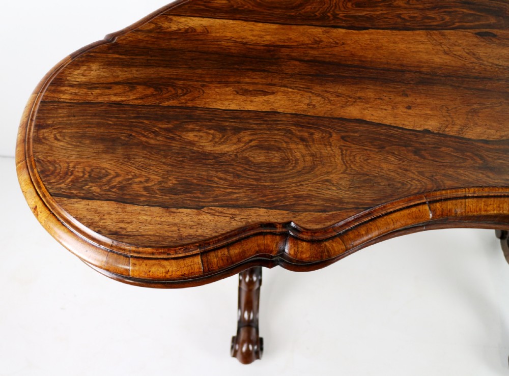 A Victorian rosewood kidney-shaped writing table with a figured timber top supported by carved lyre legs ending in scroll feet. View XIII