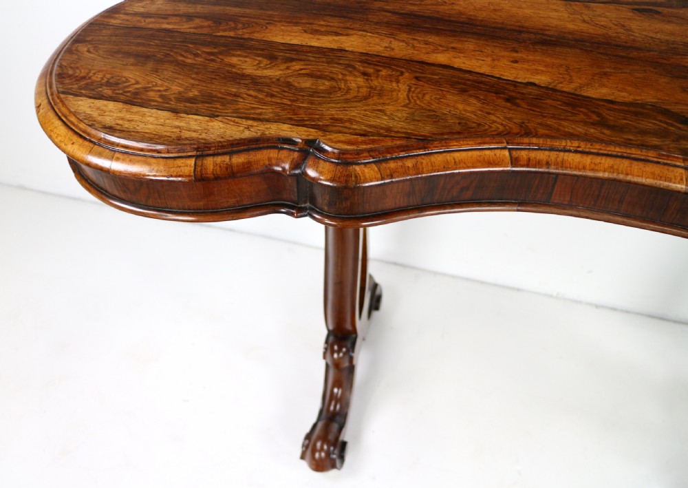A Victorian rosewood kidney-shaped writing table with a figured timber top supported by carved lyre legs ending in scroll feet. View XIV