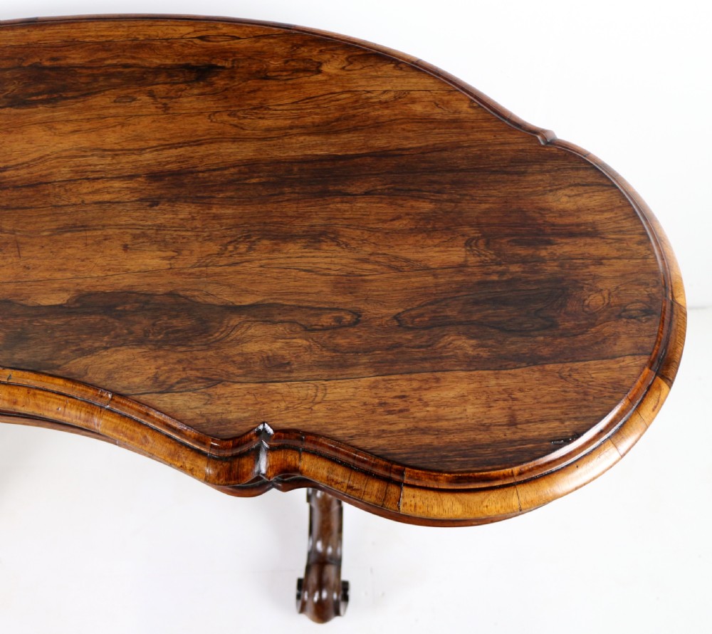 A Victorian rosewood kidney-shaped writing table with a figured timber top supported by carved lyre legs ending in scroll feet. View XV