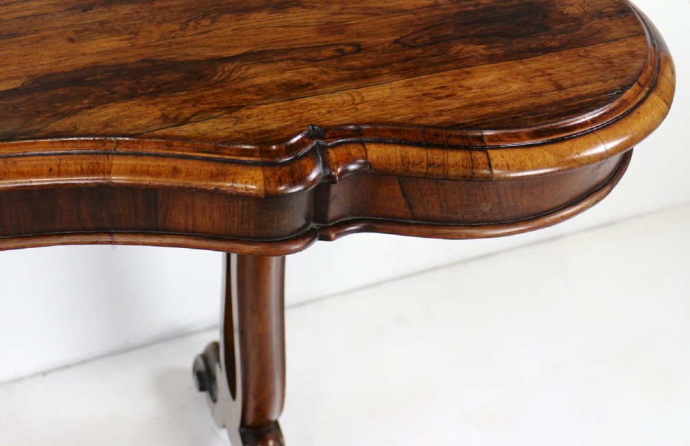 A Victorian rosewood kidney-shaped writing table with a figured timber top supported by carved lyre legs ending in scroll feet. View XVI
