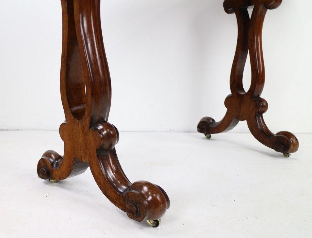 A Victorian rosewood kidney-shaped writing table with a figured timber top supported by carved lyre legs ending in scroll feet. View XX