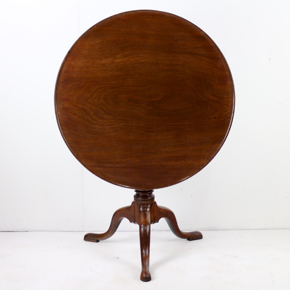 An Early Georgian mahogany tripod table featuring a circular dish top tilted vertically above a turned stem and cabriole legs with pad feet.