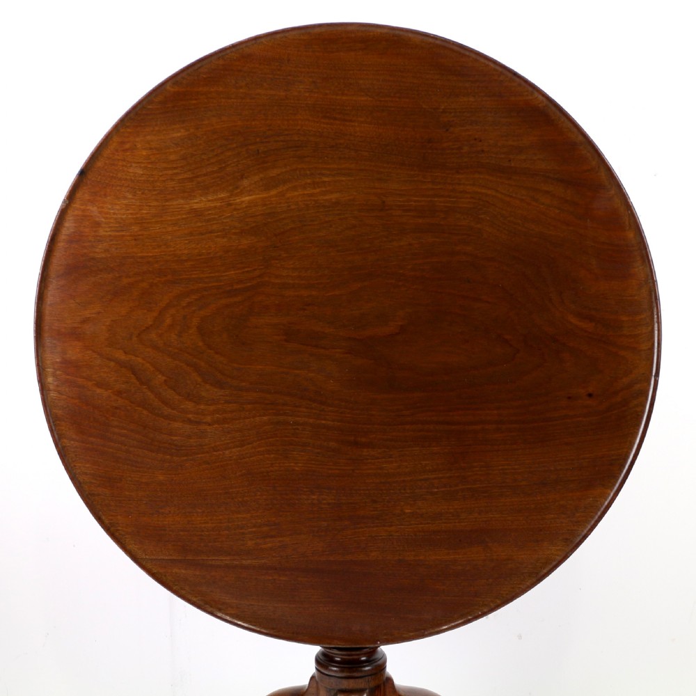 An Early Georgian mahogany tripod table featuring a circular dish top tilted vertically above a turned stem and cabriole legs with pad feet. View II