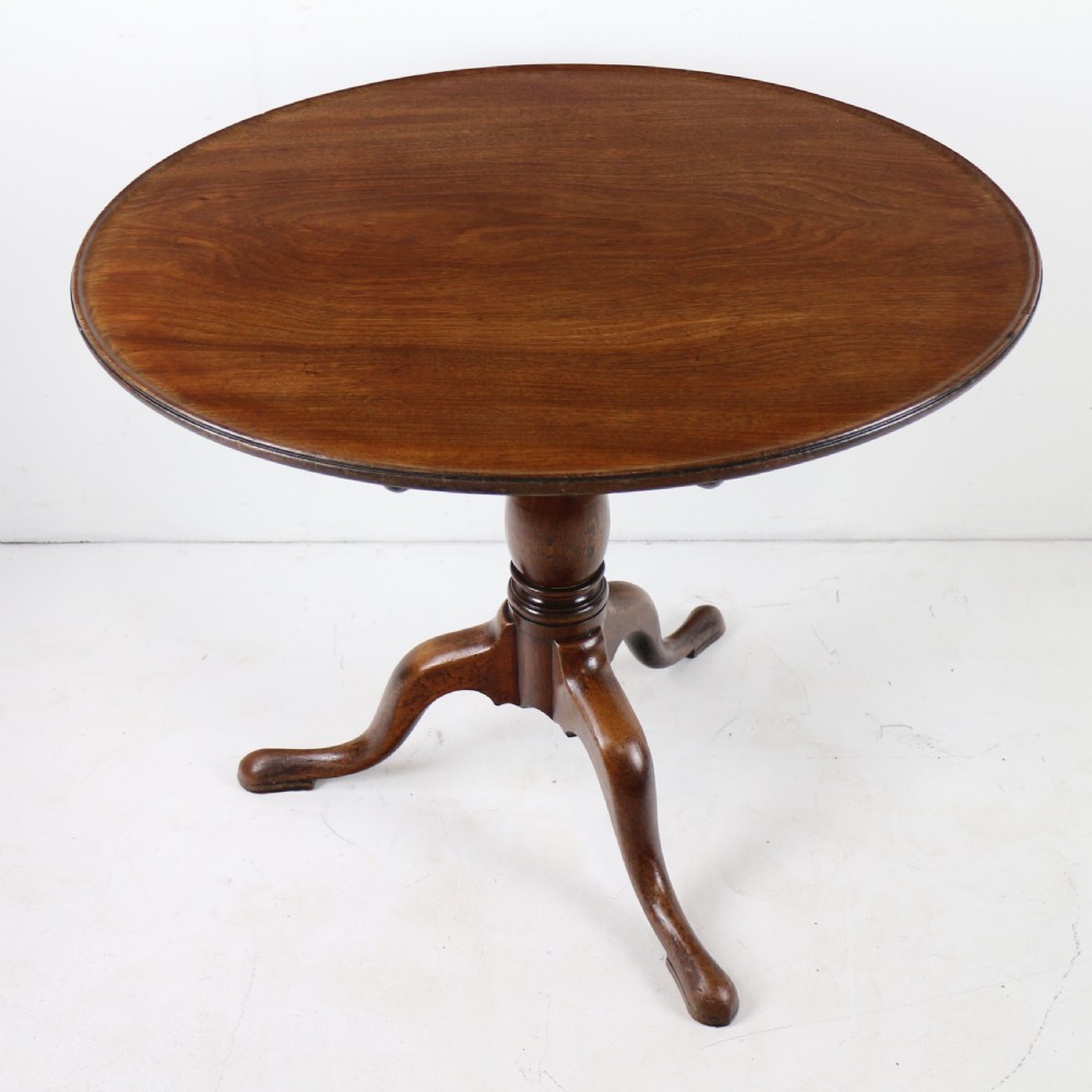 An Early Georgian mahogany tripod table featuring a circular dish top tilted vertically above a turned stem and cabriole legs with pad feet. View III