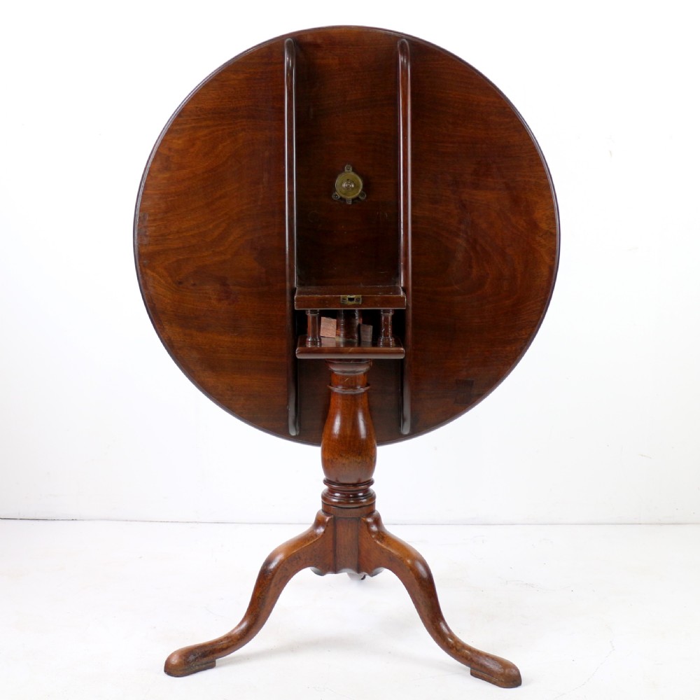 An Early Georgian mahogany tripod table featuring a circular dish top tilted vertically above a turned stem and cabriole legs with pad feet. View V