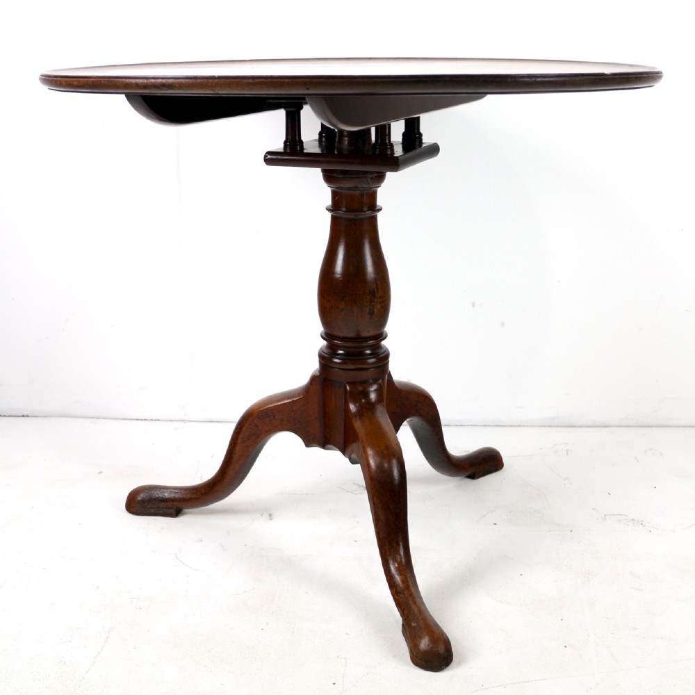 An Early Georgian mahogany tripod table featuring a circular dish top tilted vertically above a turned stem and cabriole legs with pad feet. View VI