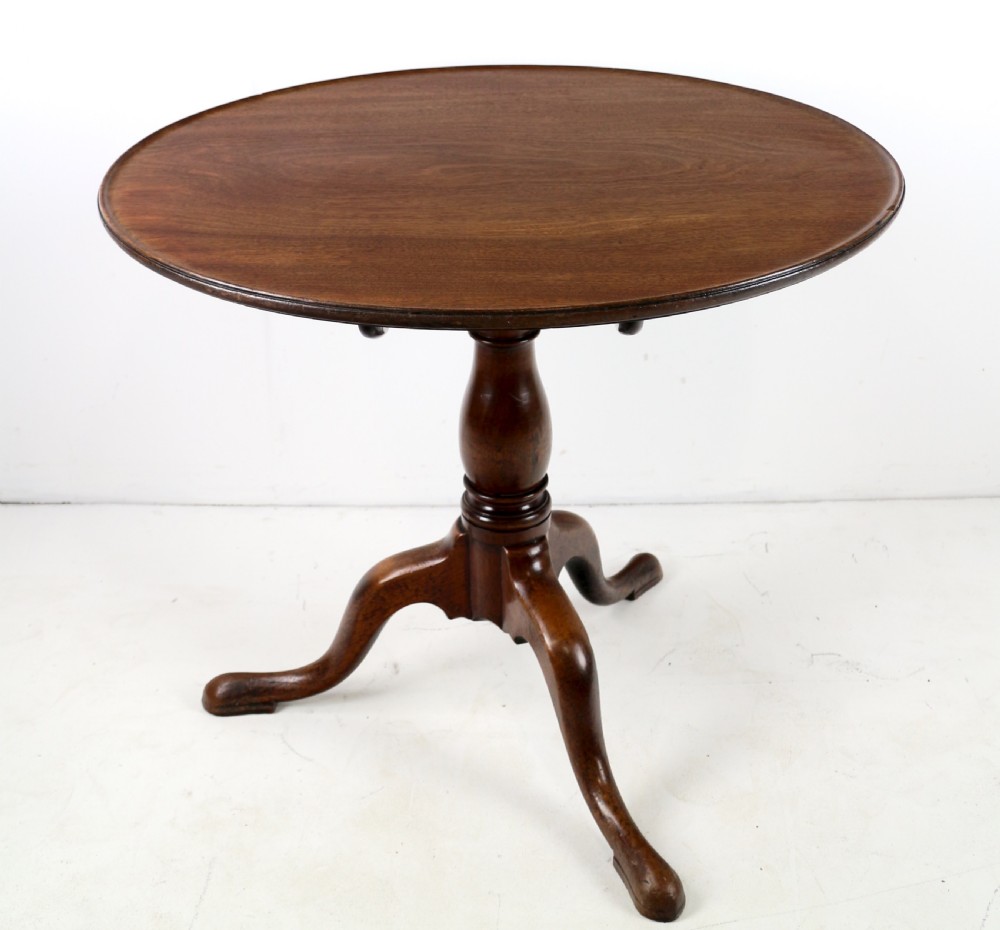 An Early Georgian mahogany tripod table featuring a circular dish top tilted vertically above a turned stem and cabriole legs with pad feet. View VII