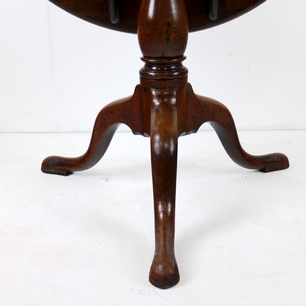 An Early Georgian mahogany tripod table featuring a circular dish top tilted vertically above a turned stem and cabriole legs with pad feet. View VIII