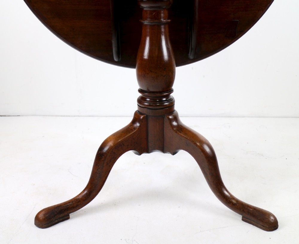 An Early Georgian mahogany tripod table featuring a circular dish top tilted vertically above a turned stem and cabriole legs with pad feet. View IX