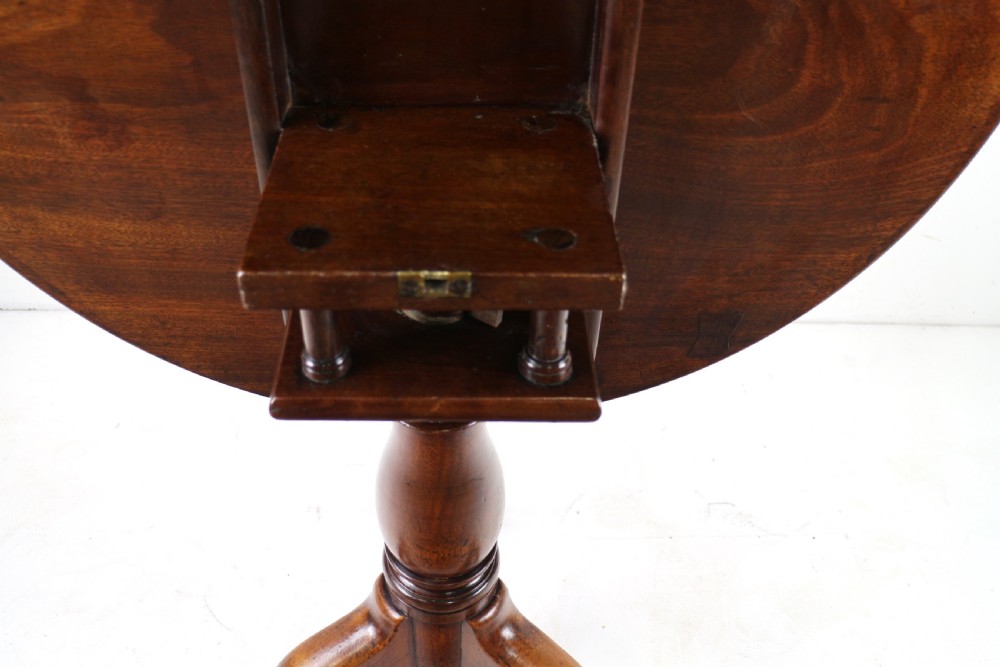 An Early Georgian mahogany tripod table featuring a circular dish top tilted vertically above a turned stem and cabriole legs with pad feet. View XII